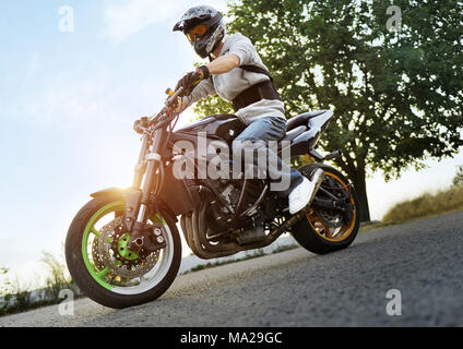 Kiev, Ukraine - 28 août 2015 : Photo de biker pose assis sur sa moto sport colorés sur la Summer Street, rempli d'éclat de coucher du soleil. Homme portant un casque de protection pour les motards. Banque D'Images