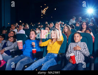 Photo d'enfants assis sur la première rangée du cinéma. Camarades très émotionnel,sorti,surpris,heureux et satisfaits. girl wearing cardigan jaune déversant jusqu'à éclater en regardant la vidéo. Banque D'Images