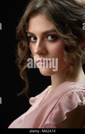 Studio portrait of attractive beatiful girl looking at camera. Modèle avoir les cheveux bouclés brun et beau yeux greeen. Femme porte à la mode robe rose. Photo a été fait sur fond noir studio. Banque D'Images