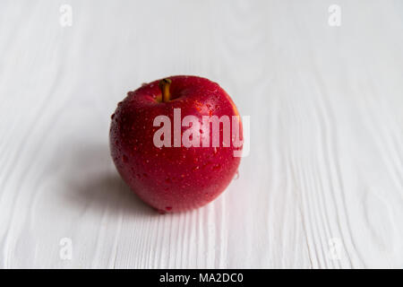 Close up fresh ripe red apple couvert de gouttes d'eau sur la surface en bois blanc Banque D'Images