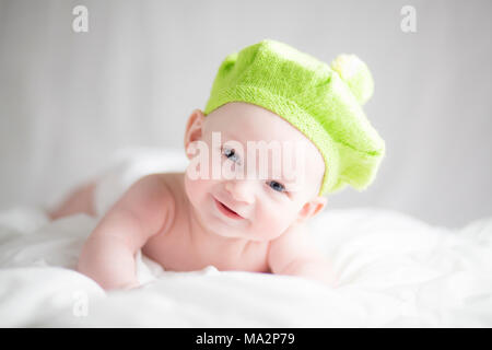 Mignon, heureux, smiling baby boy lying on bed portant un béret vert chapeau et nappy Banque D'Images