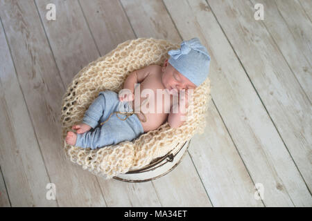 6 semaine baby boy wearing pyjamas bleu clair et couché dans un rond, godet. Tourné en studio sur un fond en bois clair. Banque D'Images