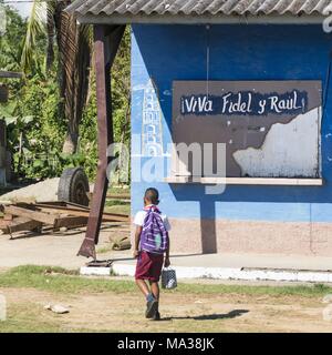 Un écolier fouines dans le soleil. Derrière lui se trouve le slogan "Vive Fidel et Raul !', peint sur le volet de la fenêtre d'une caserne à Manaca Iznaga dans la vallée des sucreries. (28 novembre 2017) | dans le monde entier Banque D'Images