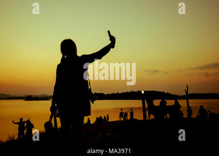 La silhouette d'une femme prise parmi la foule près de l'eau dans le coucher du soleil Banque D'Images