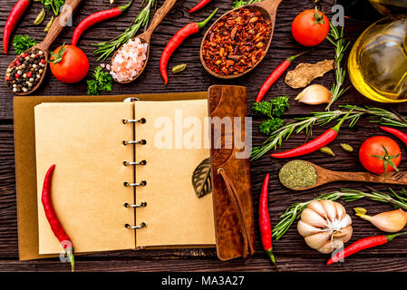 Vue d'en haut livre ouvert avec des piments, l'ail, l'huile, le vinaigre balsamique, le sel, les herbes et épices sur fond de bois. Concept de cuisson. F sélective Banque D'Images