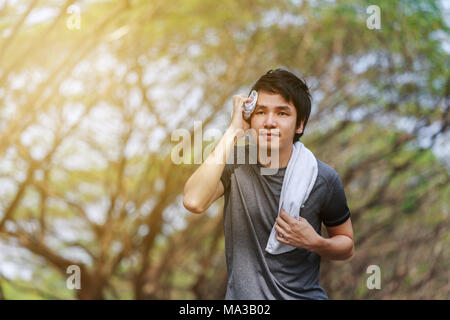 Young man running et d'essuyer sa sueur avec une serviette dans le parc Banque D'Images