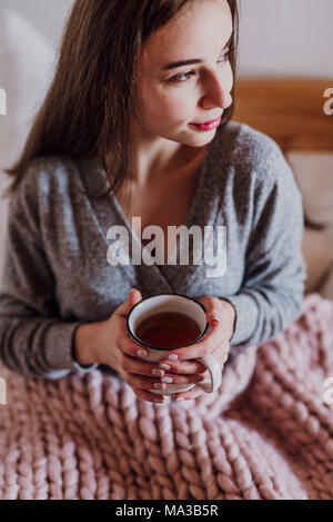 Jeune femme assise dans le lit avec une tasse de thé Banque D'Images