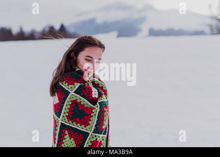 Jeune femme enveloppée dans une couverture est debout dans la neige, Banque D'Images