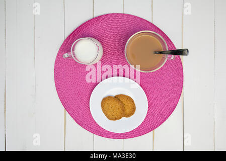 Du thé chaud, des biscuits et du lait sont disposés sur un napperon rose sur un tableau blanc, tableau. Le plateau a lait en elle. L'arrangement est centrée et tourné à partir de o Banque D'Images