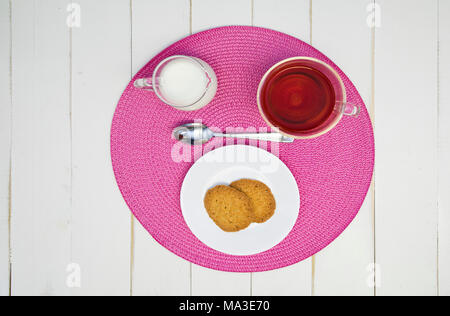Du thé chaud, des biscuits et du lait sont disposés sur un napperon rose sur un tableau blanc, tableau. L'arrangement est centrée et coup de frais généraux. Banque D'Images