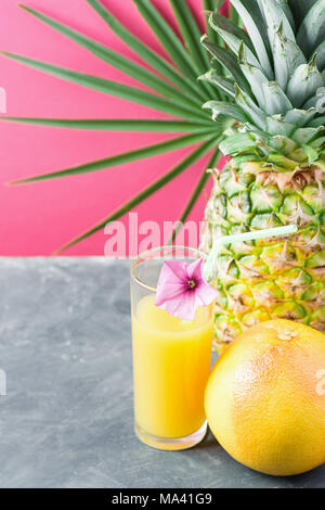 Grand verre de jus d'ananas Jus de fruits tropicaux d'agrumes avec de la paille et de fleurs. Fond rose fuchsia avec feuille de palmier. Vacances d'été Banque D'Images