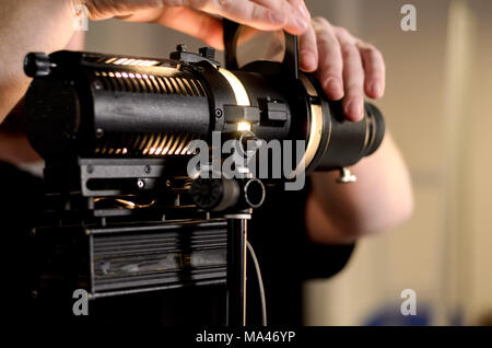 L'homme ajuste en ampoule de projecteur de film professionnel studio. Instruments de précision en action. Banque D'Images