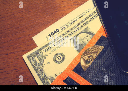 Jour de l'impôt. L'impôt sur le formulaire 1040, dollar, noir orange, noir et bitcoin wallet smartphone avec calculatrice est sur une table en bois. Banque D'Images