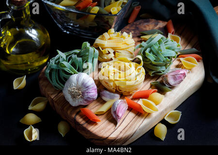 Close up noir clair-obscur avec des ingrédients pâtes spaghetti, tagliatelle et penne tricolore et l'ail et l'huile d'olive Banque D'Images