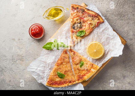 Trois morceaux de pizza aux champignons et fromage et aussi avec les tranches de citron et les feuilles de basilic sur une planche en bois recouverte de papier cuisson, servi avec t Banque D'Images