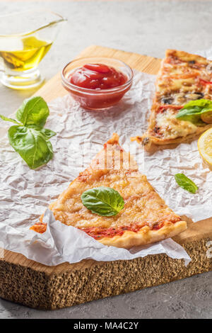 Deux morceaux de pizza aux champignons et fromage et aussi avec les tranches de citron et les feuilles de basilic sur une planche en bois recouverte de papier cuisson, servi avec Tom Banque D'Images