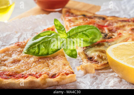 Deux morceaux de pizza aux champignons et fromage et aussi avec les tranches de citron et les feuilles de basilic sur une planche en bois recouverte de papier cuisson, servi avec Tom Banque D'Images