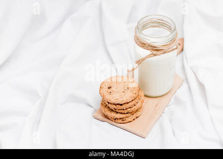 Photo d'un pot de lait et des biscuits sur une planche en bois sur un drap de lit Banque D'Images