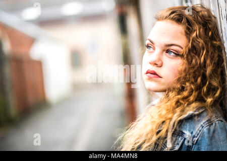 Un attrractive moody 13 jeunes adolescentes de 13 ans adolescente portant une veste en jean, dans une ruelle de la ville urbaine , Royaume-Uni Banque D'Images