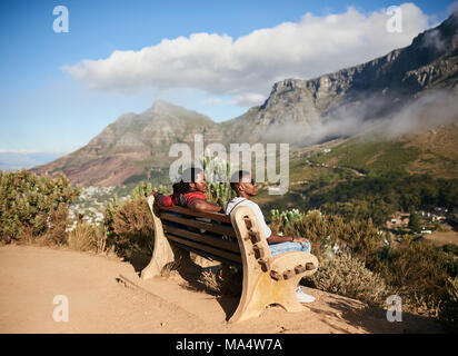 Deux hommes noirs assis ensemble sur un banc public à côté d'un sentier de randonnée avec une vue épique du terrain montagneux et mystique des nuages sur une su Banque D'Images