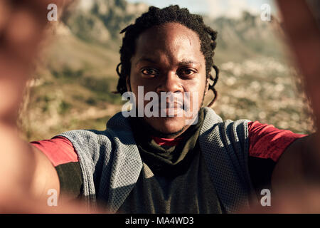 Young African guy prenant un cours d'un selfies randonnée extrême, l'échelle du côté d'une grande randonnée au coucher du soleil un soir d'été Banque D'Images