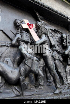 GLASGOW, ÉCOSSE - 8 janvier 2015 : un soldat sculpté d'un mémorial de guerre. Tient une petite croix en bois avec un coquelicot rouge sur elle. Banque D'Images