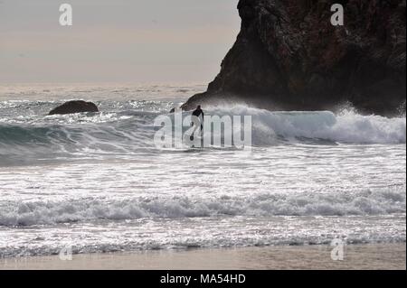 Surfer sur la vague le long de côte sauvage paysage avec l'océan Pacifique, les vagues et les falaises rocheuses, rétro-éclairé spray salé dans Big Sur, Californie, USA. Banque D'Images