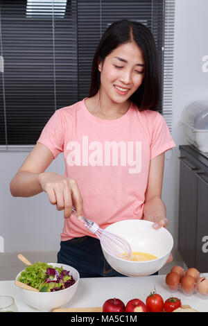 La cuisine et femme en fouettant les oeufs dans un bol dans la cuisine prix Banque D'Images