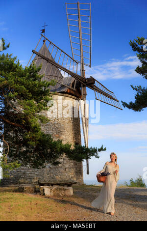 Fille blonde en robe blanche transportant un panier de lavande sous un moulin à vent, valensole, Provence, France Banque D'Images