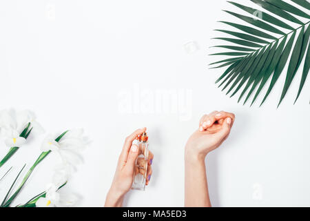 Vue du dessus de la main de femme manucure rose parfum de pulvérisation du poignet entre les branche de palmier et iris fleurs sur fond blanc. Une élégante télévision jeter fra Banque D'Images