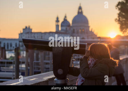 Petite fille à travers le télescope le Grand Canal, dans le contexte de la Basilica di Santa Maria della Salute, Sainte Marie de la santé au coucher du soleil, Venise, Vénétie, Italie Banque D'Images