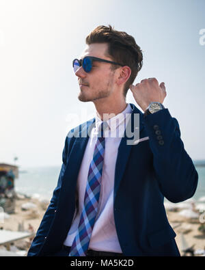 Jeune homme élégant en costume élégant et sunglass sur fond de mer et ciel. Guy est réussie en plein air relaxant chaude journée ensoleillée. Guy branché Banque D'Images