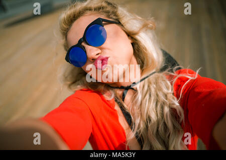 Close-up view of young Beautiful woman en robe rouge vif montre un baiser au front de mer de la ville. Elegant blonde fille avec joli visage sur la promenade en bois Banque D'Images