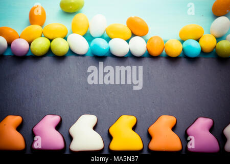 Joyeuses Pâques. Les lapins de chocolat colorés dans une rangée de petits oeufs doux pastel sur planche à découper ardoise fond bleu noir. Vue d'en haut. Copyspace Banque D'Images