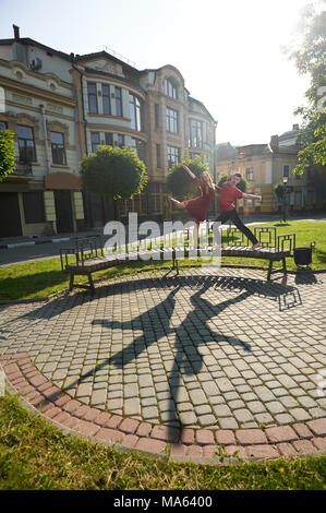 Ivano-Frankivsk, Ukraine - 1 juin 2015 : beau jeune couple danse sur banc de la ville à proximité de plantes vertes et de façade du bâtiment d'origine. Garçon et fille à heureux, satisfaits et émotionnel. Banque D'Images