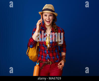 La recherche de lieux d'inspiration. surpris adventure excited woman randonneur dans une chemise à carreaux à l'aide d'un smartphone isolé sur blue Banque D'Images