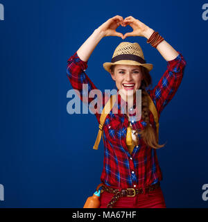 La recherche de lieux d'inspiration. heureux sain traveller femme dans une chemise à carreaux en forme de cœur montrant mains isolé sur blue Banque D'Images