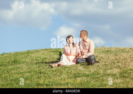 Jeune couple d'amoureux assis sur l'herbe sur une colline. Banque D'Images