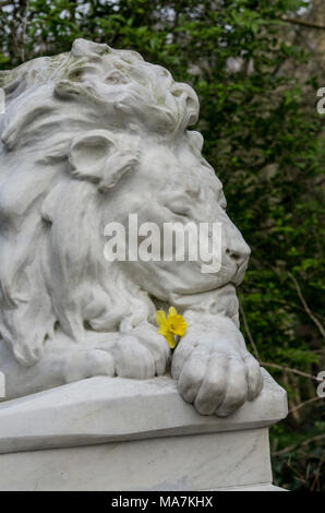 Statue d'un lion mâle see fermé expression pacifique tenant une jaune jonquille au cimetière abney park, Stoke Newington, Hackney, Londres, Angleterre, RU Banque D'Images