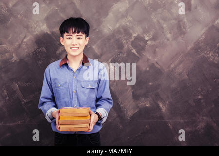 Beau jeune homme asiatique holding livre sur le mur grunge smiley looking at camera Banque D'Images