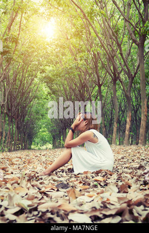 Femme triste les mains sur son visage si tristement assis sur feuille sèche dans la forêt Banque D'Images