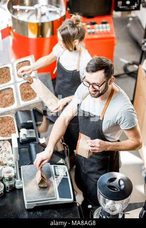 Deux vendeurs en uniforme et d'un poids de remplissage de sacs de café dans le magasin de café. Vue de dessus Banque D'Images