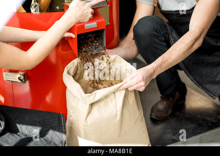 Verser les grains de café torréfiés dans le sac en papier de la machine torréfacteur pour vendre Banque D'Images