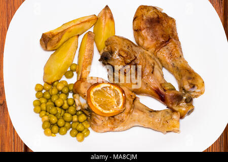 Pilons de poulet rôti avec des pommes de terre et les pois verts sur plaque sur fond de bois, vue du dessus. Banque D'Images