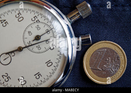 Pièce en euros avec une valeur nominale d'un euro et le chronomètre sur la vieille toile de jeans bleu - business background Banque D'Images