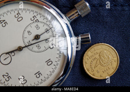 Pièce en euros d'une valeur nominale de 10 centimes d'euro (côté arrière) et un chronomètre sur la vieille toile denim bleu - business background Banque D'Images