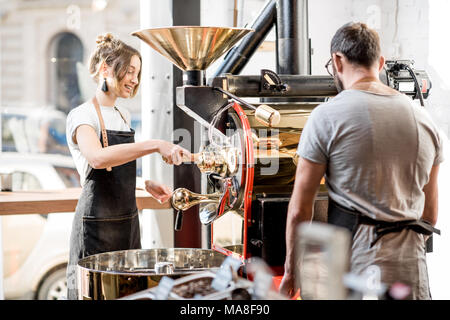 L'homme et la femme en uniforme qui travaillent avec machine à café en grains torréfaction torréfacteur au café Banque D'Images