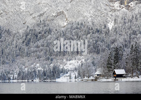 Petite cabane au pied d'un lac avec la forêt enneigée et les montagnes en arrière-plan Banque D'Images