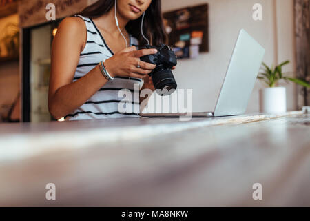 La regardant blogger femme photo reflex numérique tout en travaillant sur son ordinateur portable à la maison. Femme assise devant son ordinateur portable avec une exploitation d'écouteurs Banque D'Images