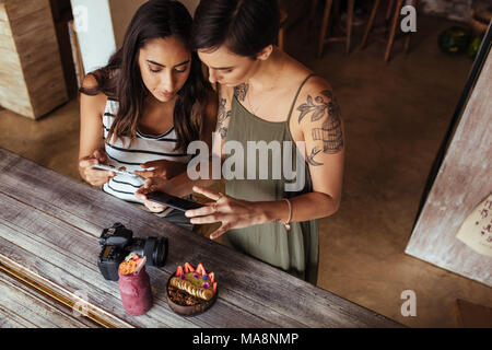 Les blogueurs alimentaire prise de photos pour leur blog en utilisant les téléphones mobiles. Photos de tournage blogueurs femmes coupe de fruits et jar smoothie placés le long d'une Banque D'Images